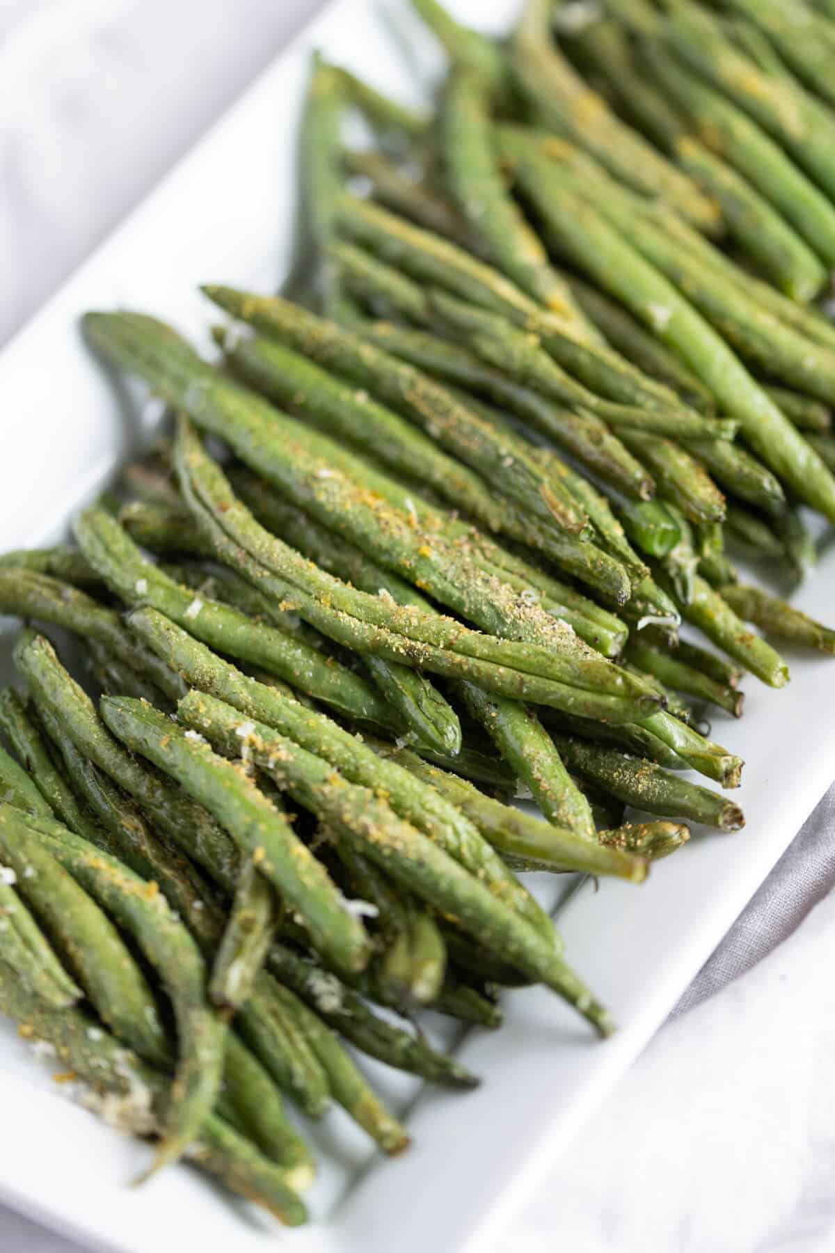 crisp air fried green beans well seasoned on a white serving dish.