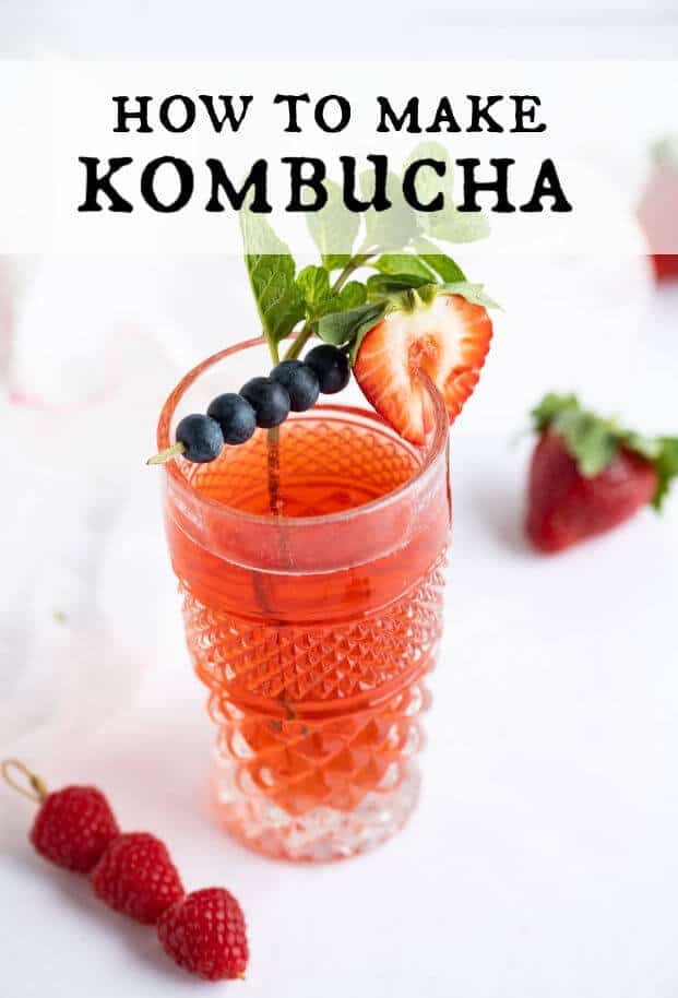 Berry flavored kombucha in a decorative tall glass garnished with a cocktail skewer of blueberries, a sliced strawberry, and a sprig of mint leaves. via @artfrommytable