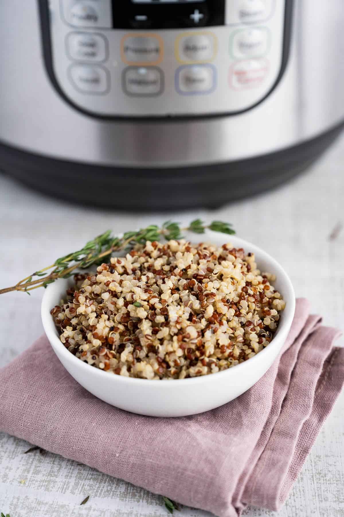 Cooked quinoa in a white serving dish in front of a pressure cooker.