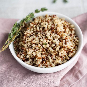 Tri-color quinoa in a round white serving bowl garnished with a sprig of fresh thyme.