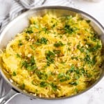 Cooked spaghetti squash in a skillet with toasted pine nuts and fresh herbs.