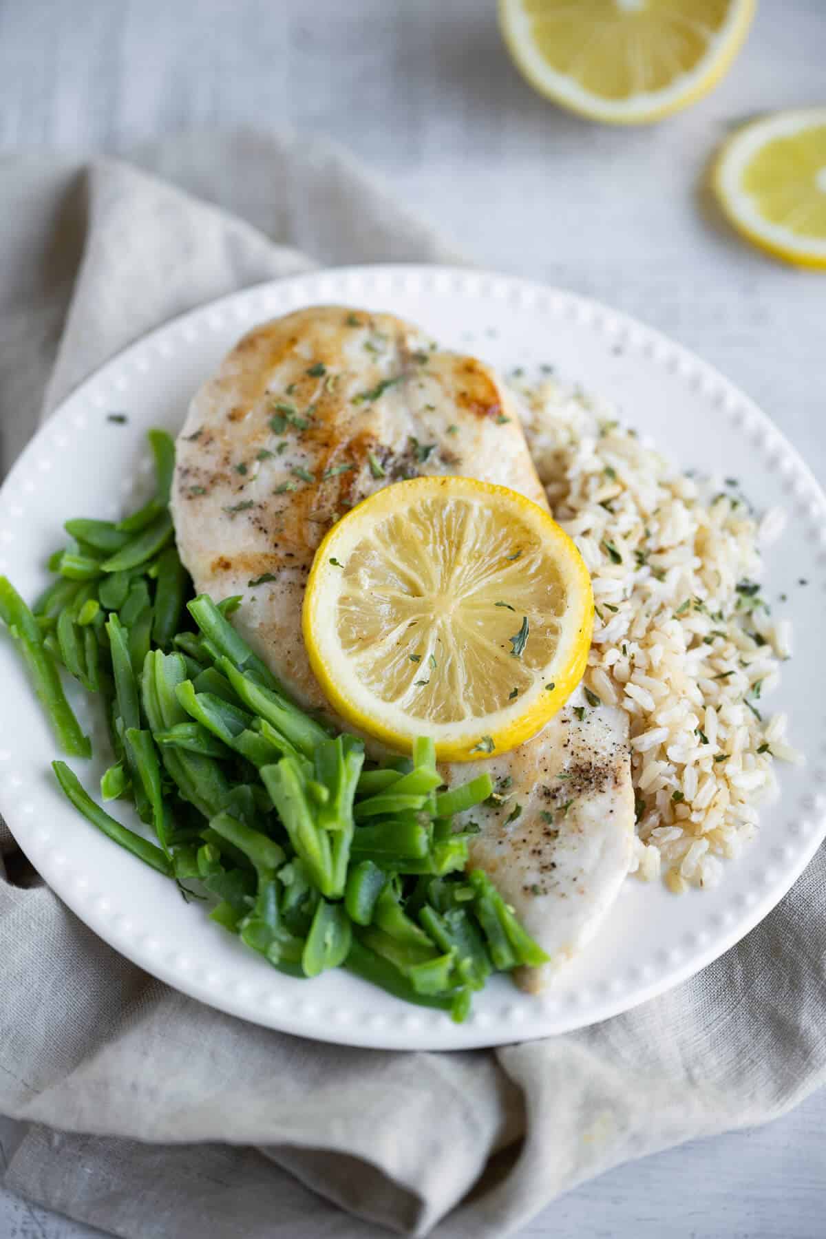 Chicken breast, cooked sous vide method, on a plate with green beans and rice. Chicken is garnished with a lemon slice.