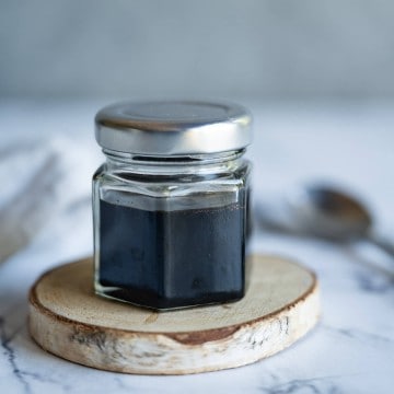 Balsamic reduction in a glass jar with a lid, spoon in the background.
