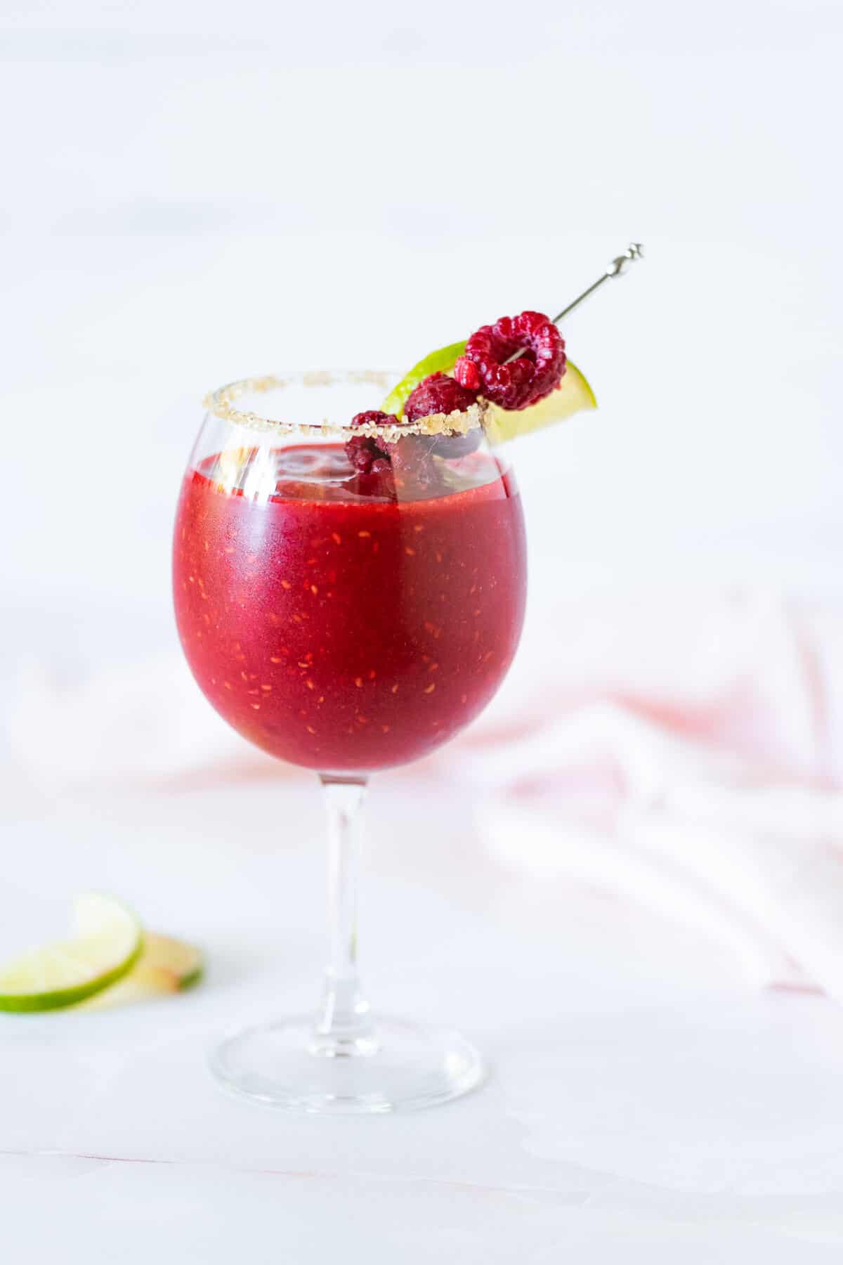 Virgin Raspberry Daiquiri in a stemmed glass with sugar on the rim and garnished with raspberries and a lime wedge.