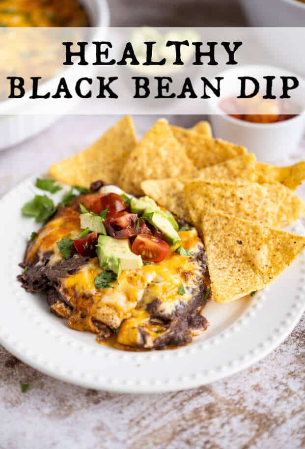 Warm black bean dip topped with melted cheese, cilantro, diced tomato and diced avocado, on a white plate with a side of tortilla chips. via @artfrommytable