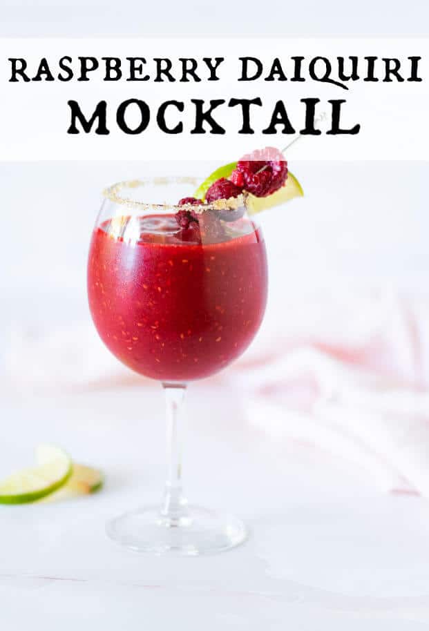 Frozen Raspberry Daiquiri Mocktail in a stemmed glass rimmed with sugar and garnished with fresh raspberries and lime wedge on a cocktail pick. via @artfrommytable