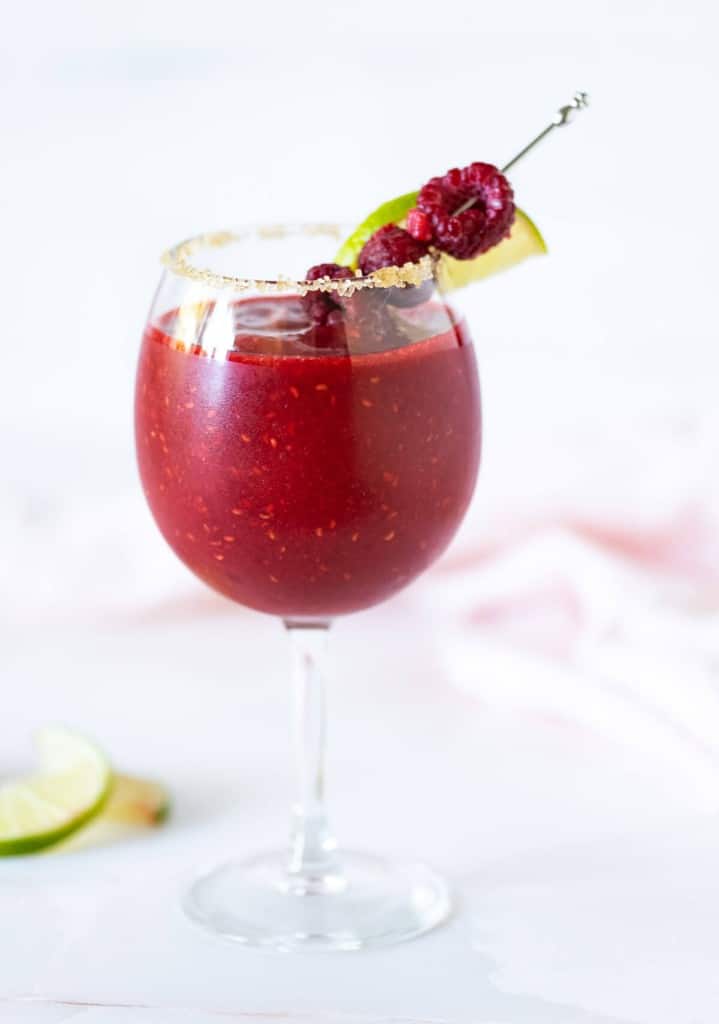 Frozen Raspberry Daiquiri Mocktail in a stemmed glass rimmed with sugar and garnished with fresh raspberries and lime wedge on a cocktail pick.