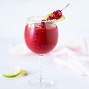 Frozen Raspberry Daiquiri Mocktail in a stemmed glass rimmed with sugar and garnished with fresh raspberries and lime wedge on a cocktail pick.