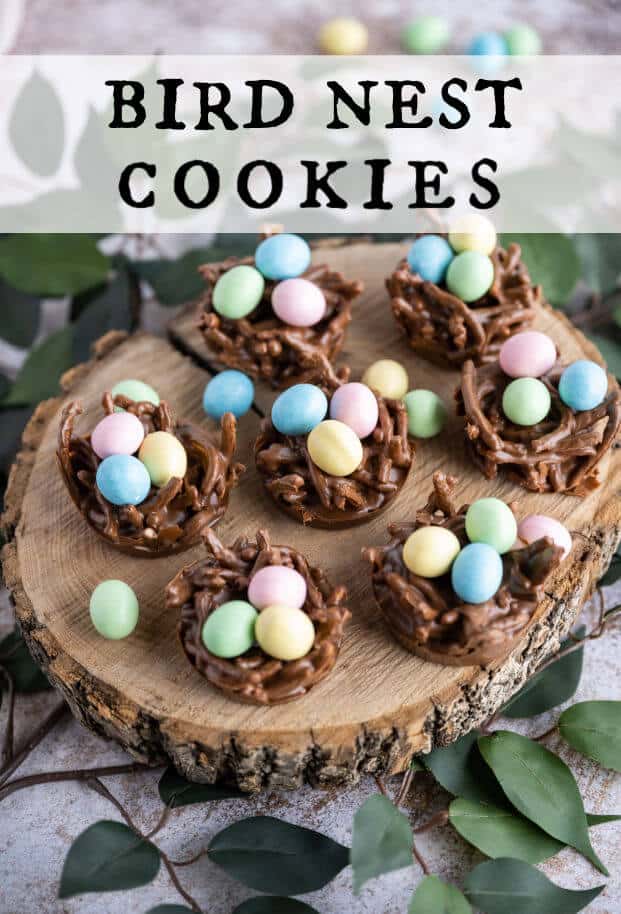 A group of chocolate birds nests filled with mini candy coated eggs on a wooden serving platter surrounded with greenery. via @artfrommytable