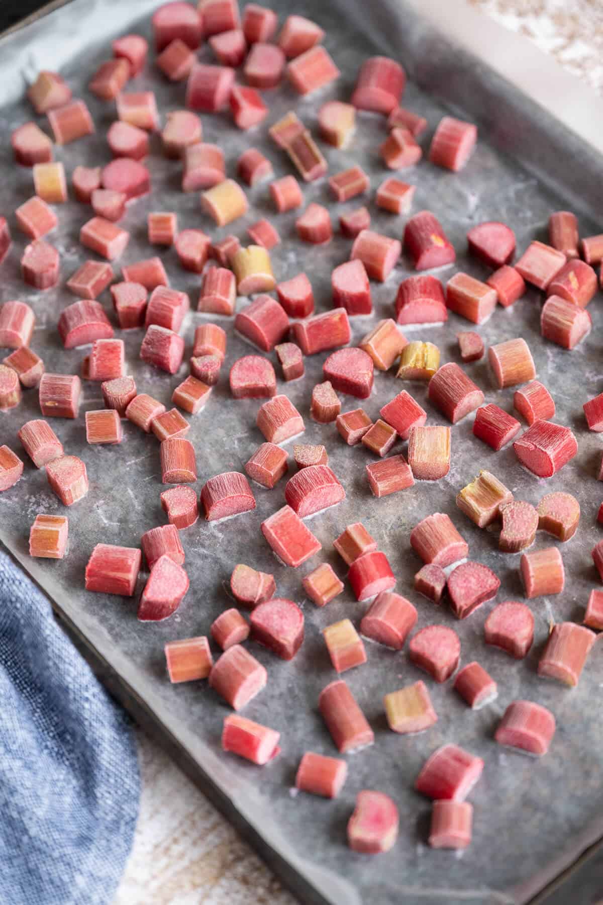Pieces of frozen rhubarb on a wax paper lined rimmed baking sheet.