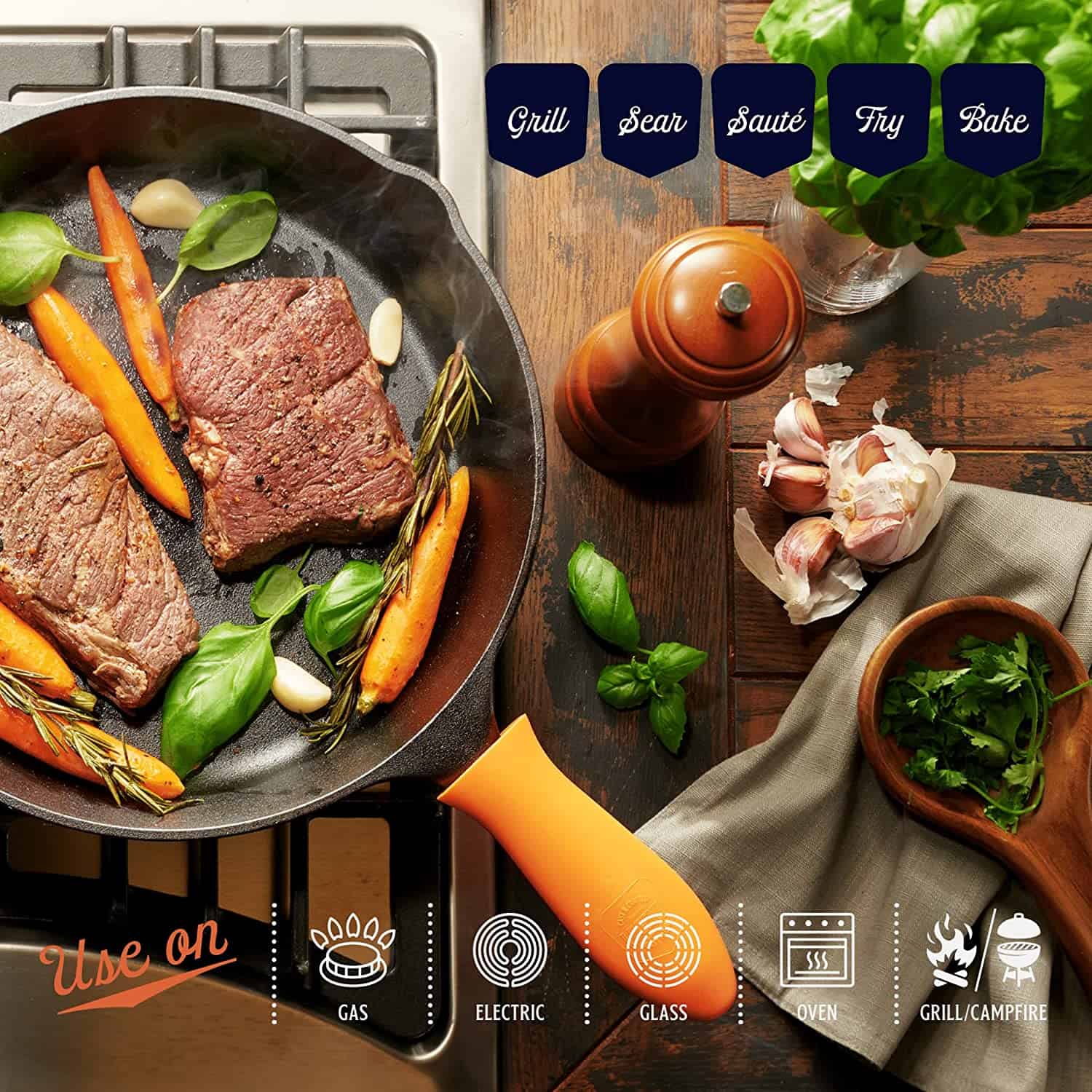Legend Cast Iron Skillet on a stove cooking steak. Also in the pan are a few carrots and some fresh herbs. This pan has an orange silicone handle cover.