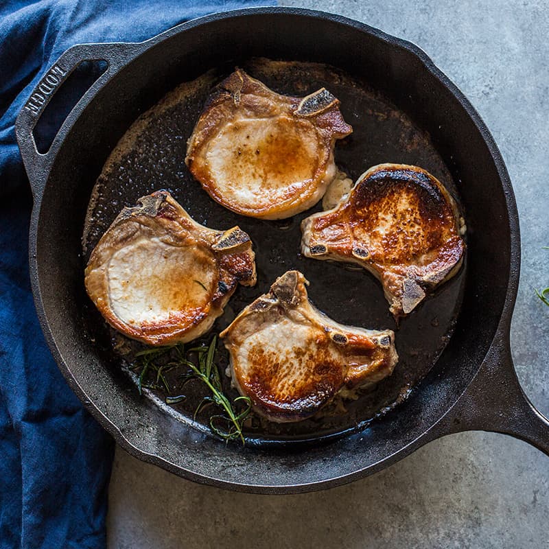 Lodge Cast Iron pan with cooked and seared pork chops inside.