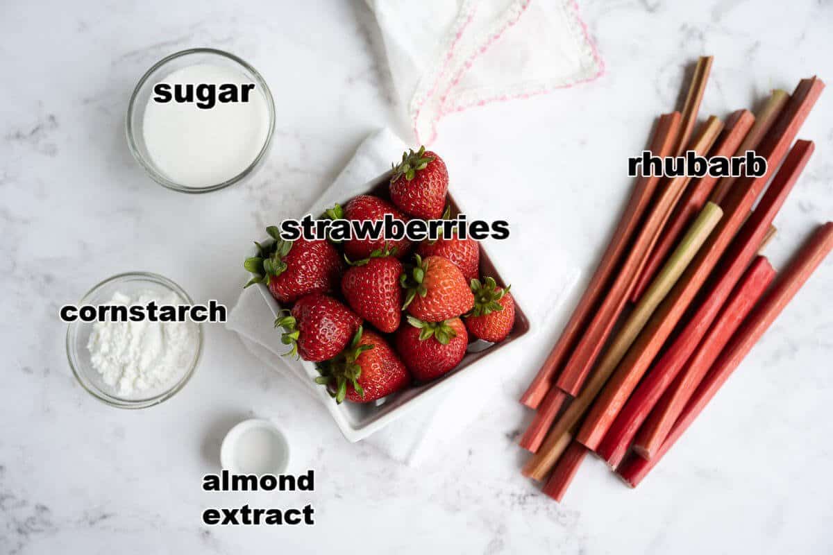 Ingredients to make rhubarb strawberry crisp filling: strawberries, rhubarb, sugar, cornstarch, and almond extract.