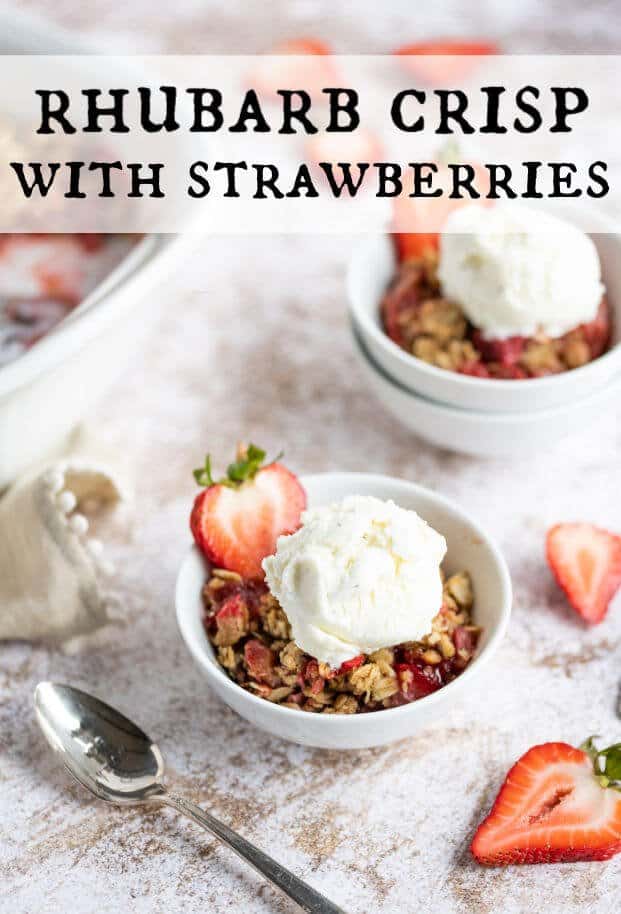 2 bowls of Rhubarb Crisp with strawberries topped with a scoop of ice cream. Each bowl is garnished with a fresh strawberry slice. A spoon is alongside one of the bowls. via @artfrommytable