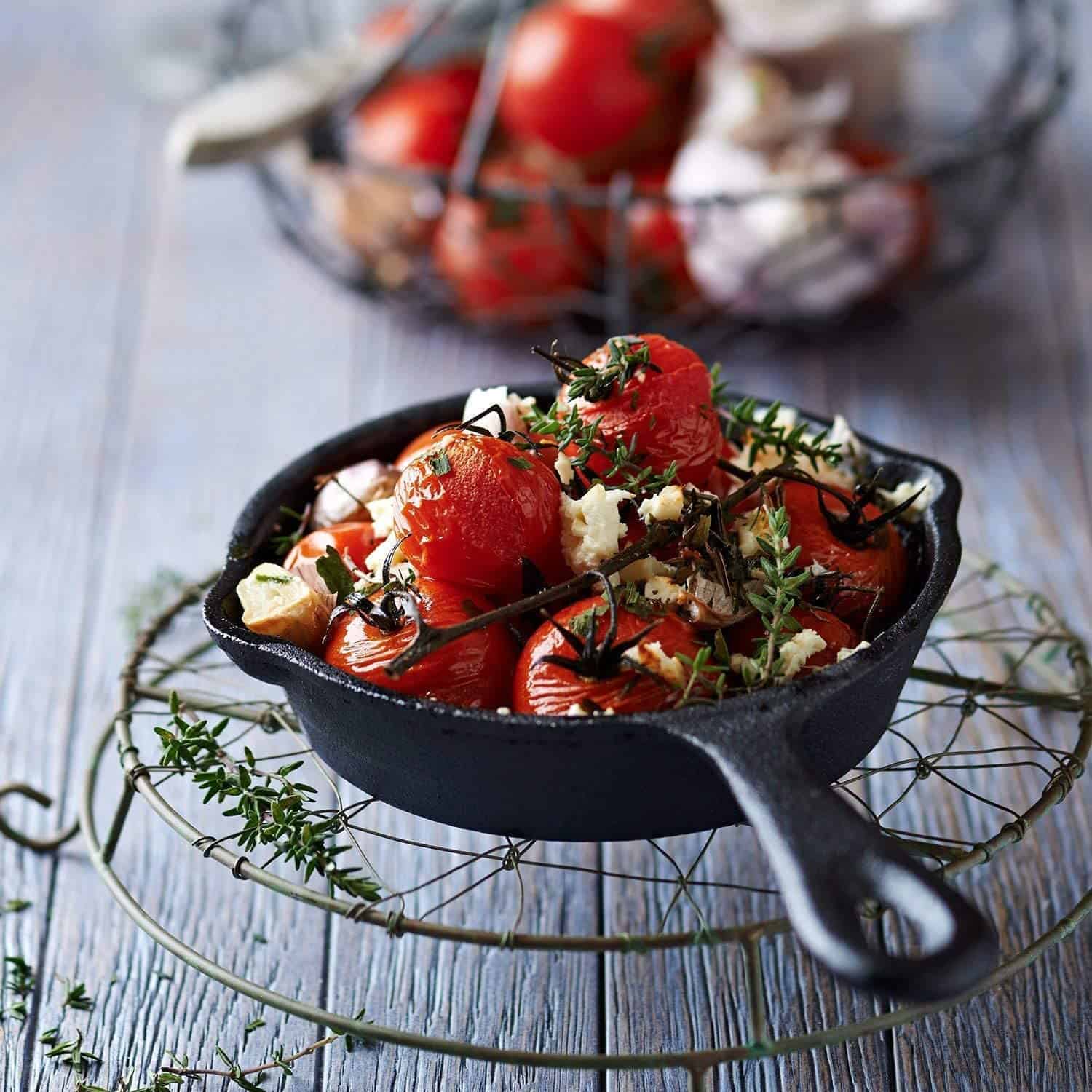 Mini cast iron pan from Simple Chef full of roasted cherry tomatoes on the vine, topped with herbs and crumbled cheese.
