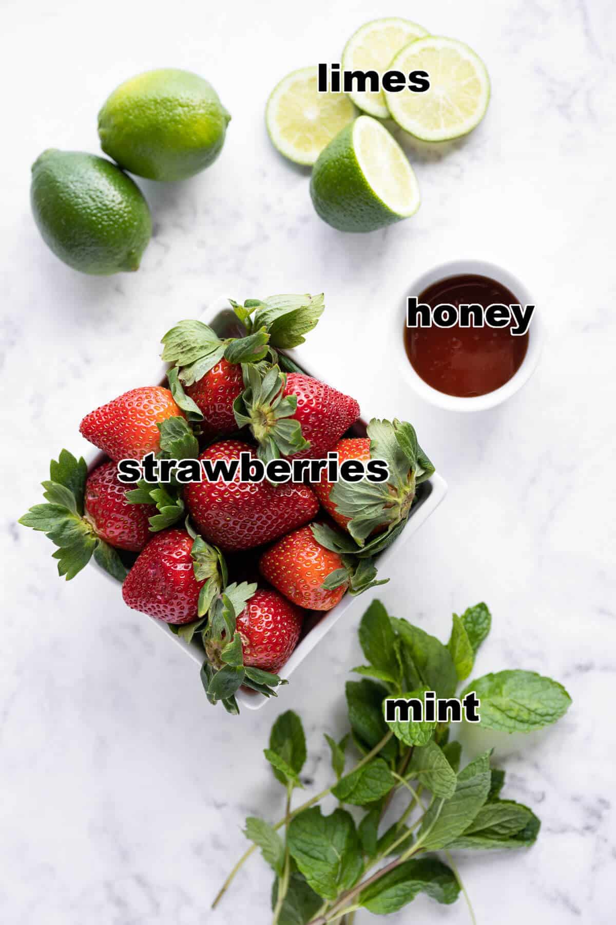Ingredients for a strawberry mocktail: limes, strawberries, honey, and mint.