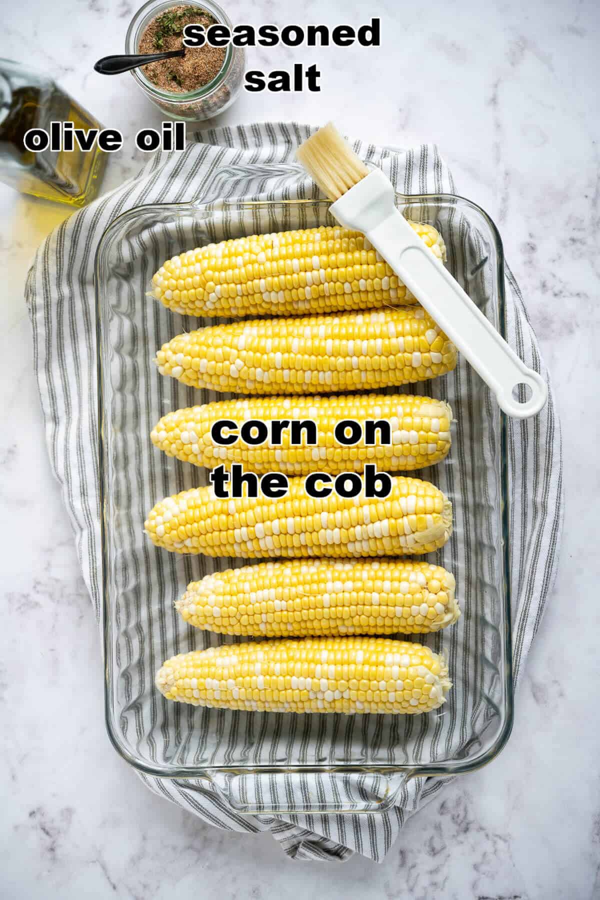 6 ears of raw corn on the cob in a 9x13 dish, bottle of olive oil, a jar of seasoned salt, and a pastry brush.