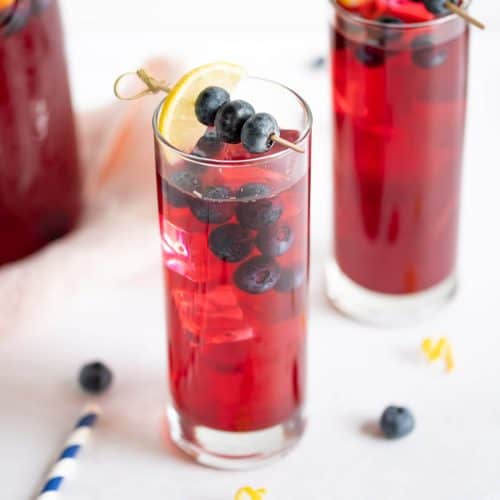 2 tall glasses of blueberry lemonade, garnished with fresh blueberries and lemon slices.