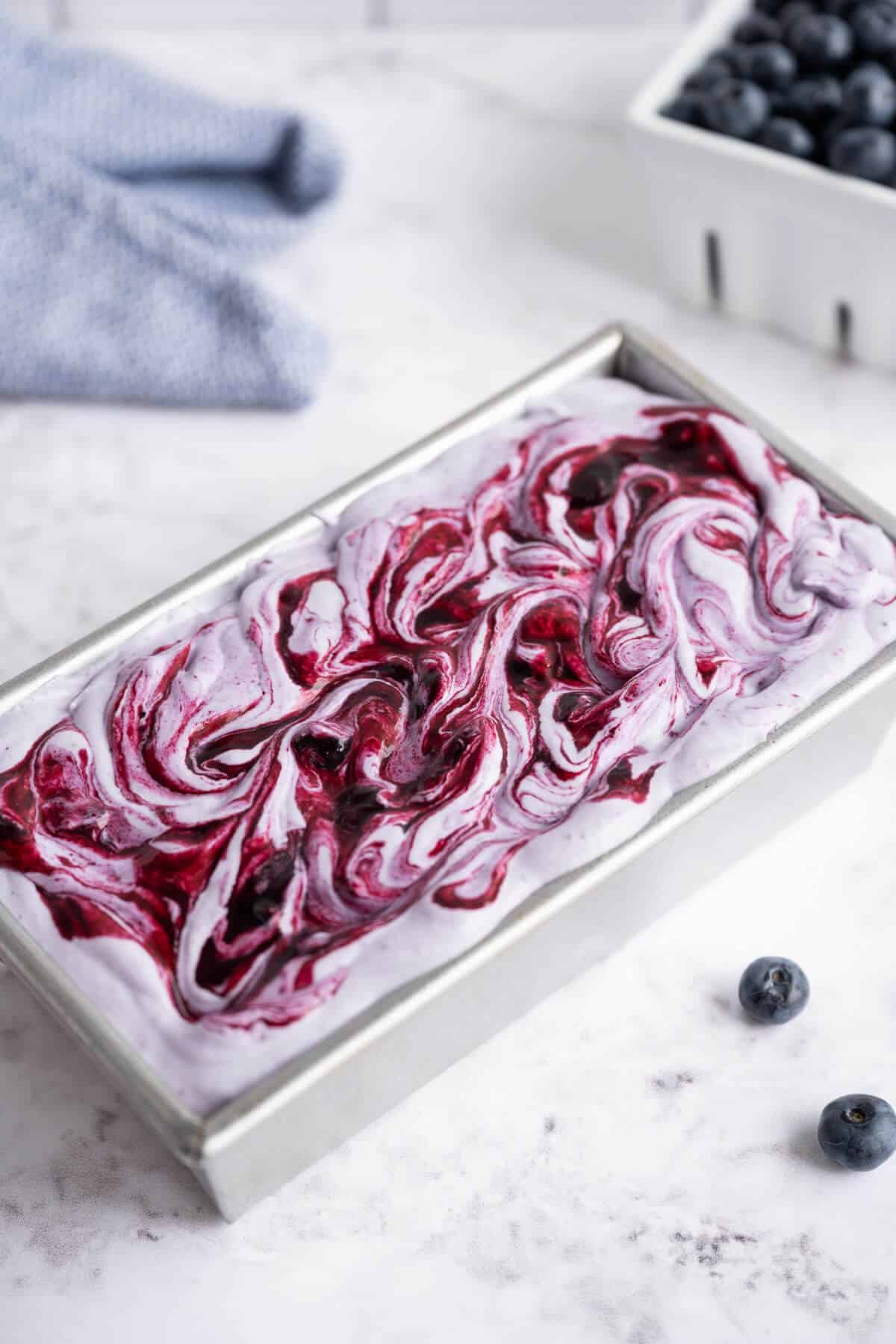 Blueberry Ice Cream Mixture in a loaf pan ready to freeze. The top has blueberry sauce swirled in.