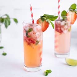 2 glasses of freshly made strawberry mojito mocktails. Drinks are garnished with fresh mint leaves and sliced strawberries. Each glass has a red and white striped straw in it.