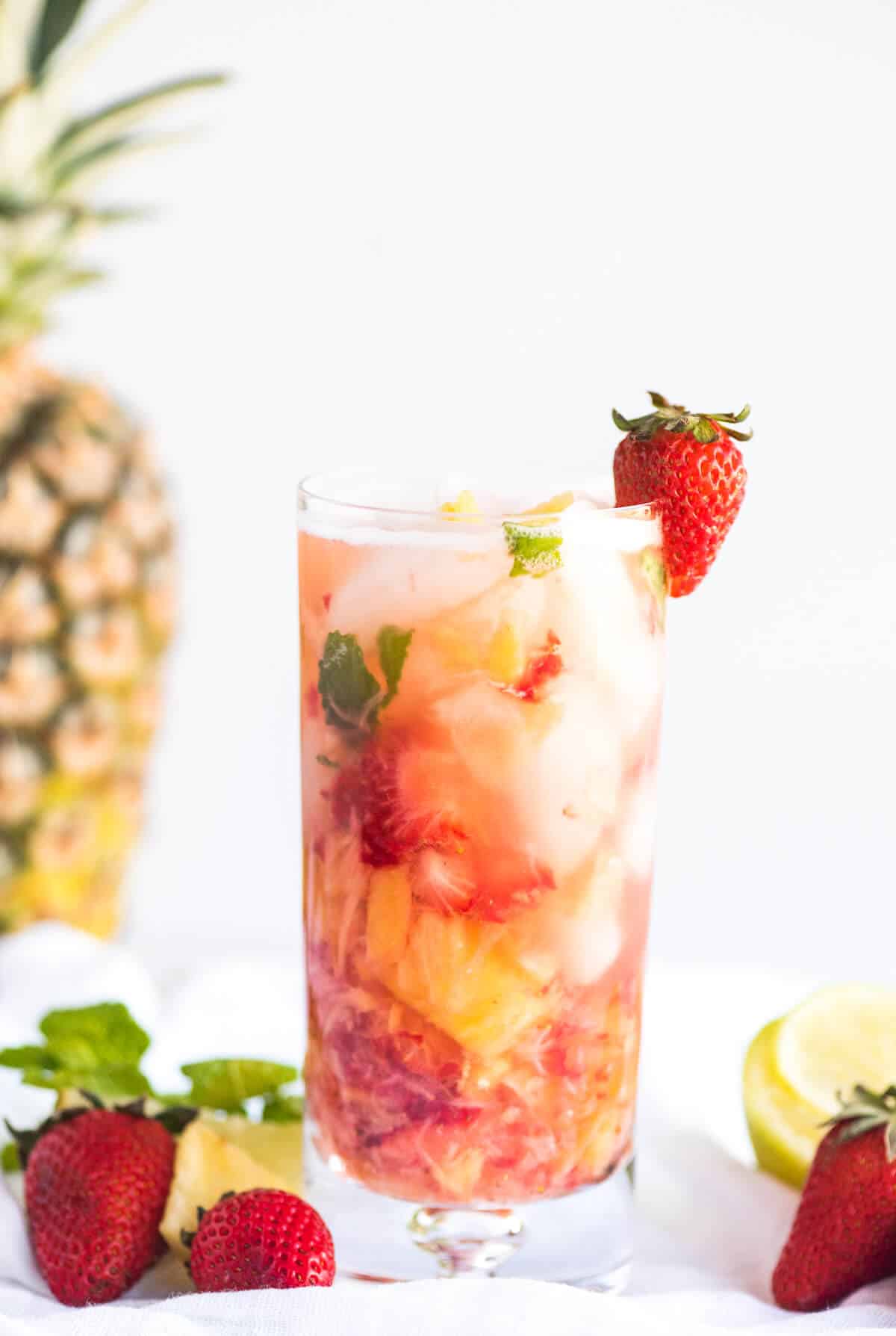 Muddled strawberries, pineapple and mint topped with sparkling water in a clear tall glass.