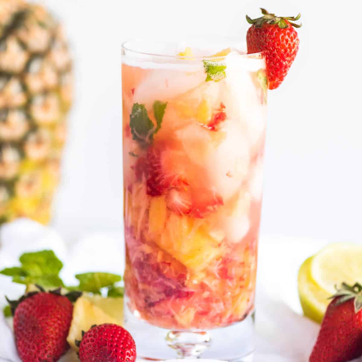 Strawberry Pineapple Mojito in a tall clear glass with ice, garnished with a fresh strawberry.