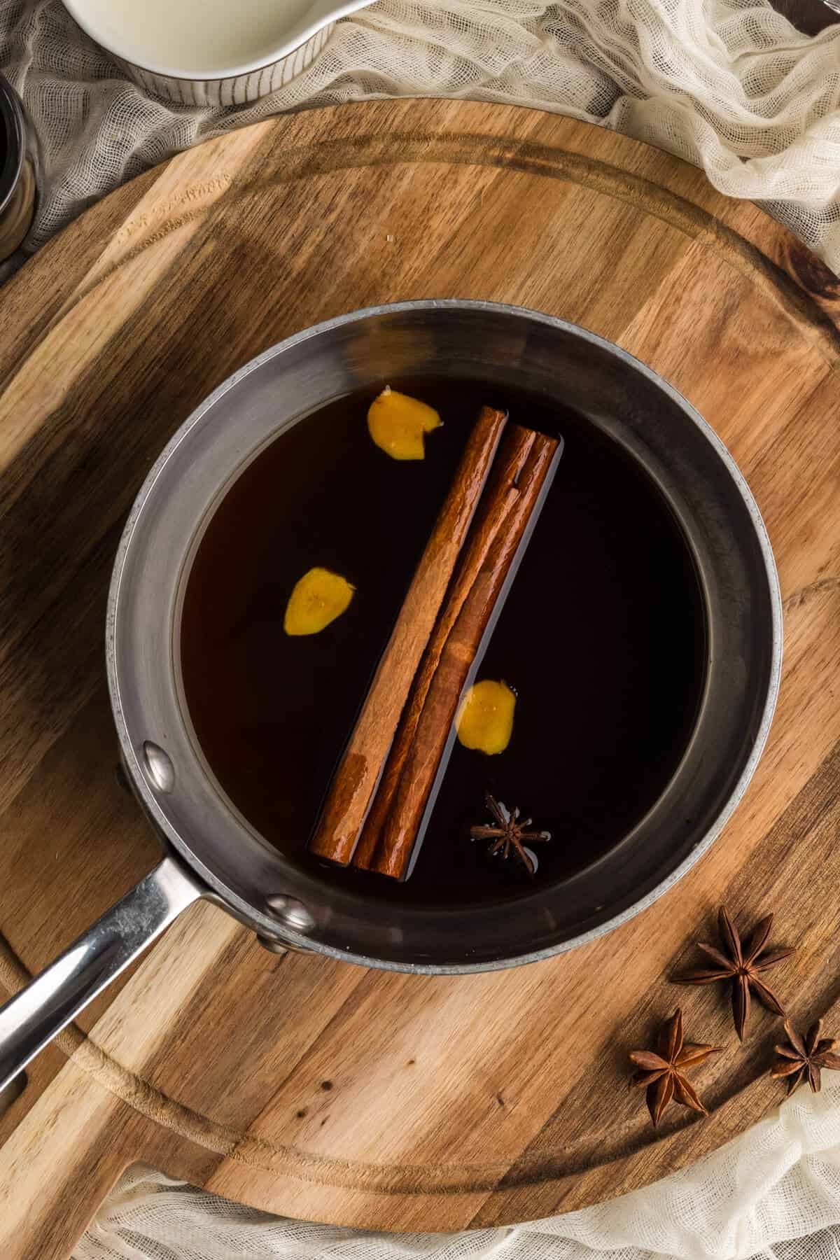 Homemade Gingerbread syrup simmering in a saucepan. Slices of fresh ginger, cinnamon sticks, and star anise are floating on top.