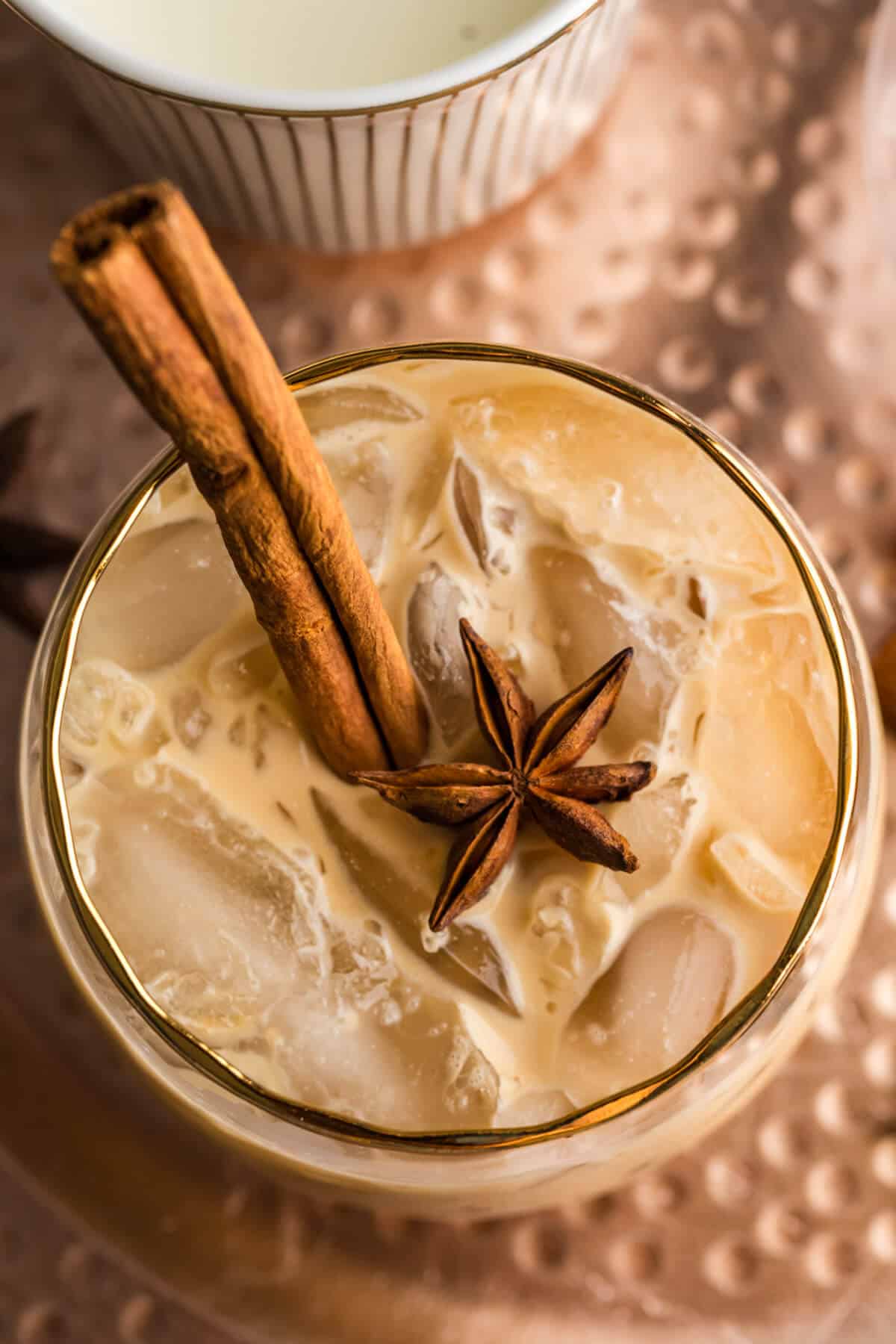 Overhead view of a virgin Gingerbread White Russian in a gold rimmed cocktail glass garnished with a cinnamon stick and a whole star anise.