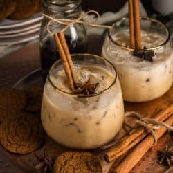 Two Gingerbread White Russian Mocktails in gold rim glasses, served on a platter surrounded by gingersnap cookies and cinnamon sticks.