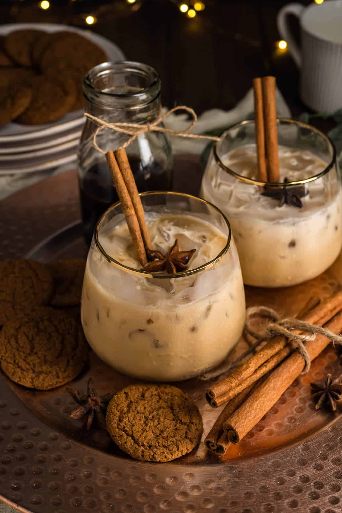 Two Gingerbread White Russian Mocktails in gold rim glasses, served on a platter surrounded by gingersnap cookies and cinnamon sticks.