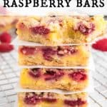 Stack of Raspberry Bars on a baking rack. The bars are separated with parchment paper. A few raspberries around the bars.