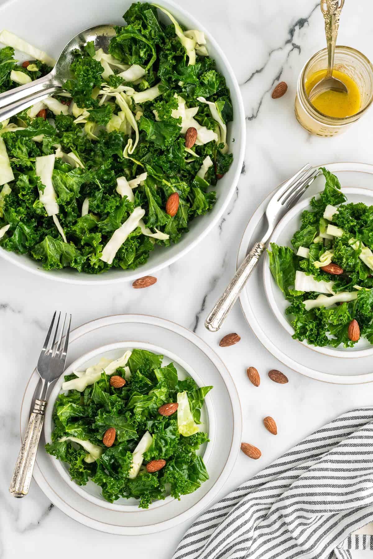 Kale Crunch Salad in a serving bowl and two plates beside it with salad on each plate.