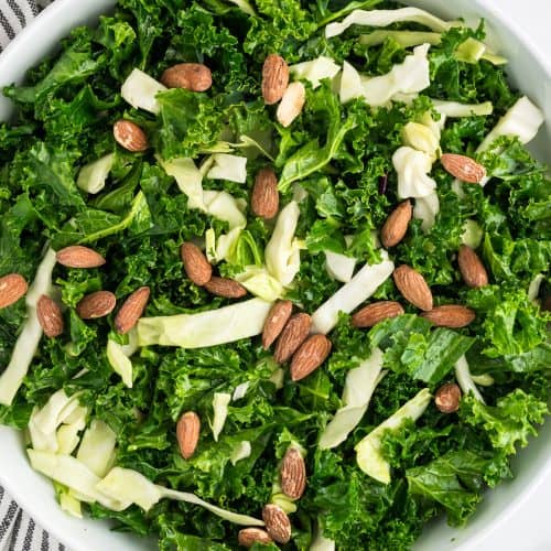 A white bowl filled with Kale Crunch Salad, garnished with roasted almonds.
