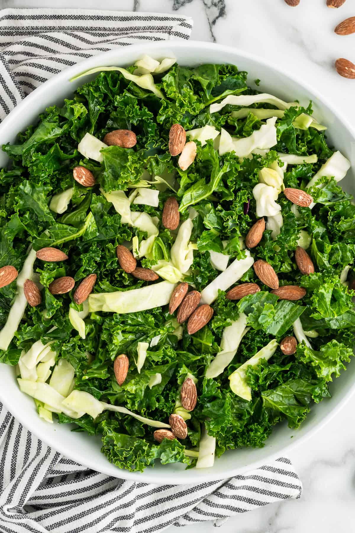 A white bowl filled with Kale Crunch Salad, garnished with roasted almonds. 