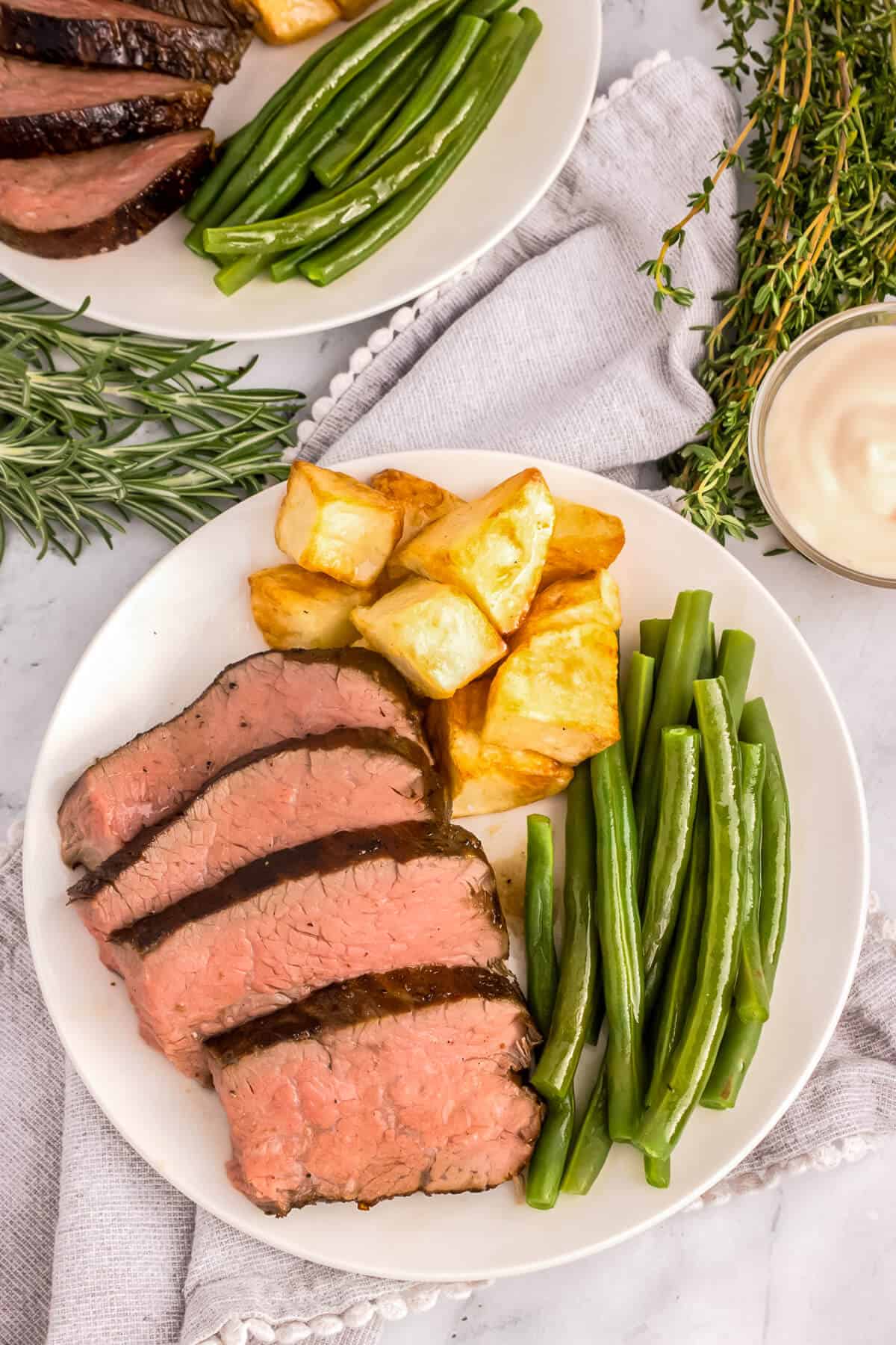 Sliced tri-tip roast on a plate with green beans and diced potatoes.