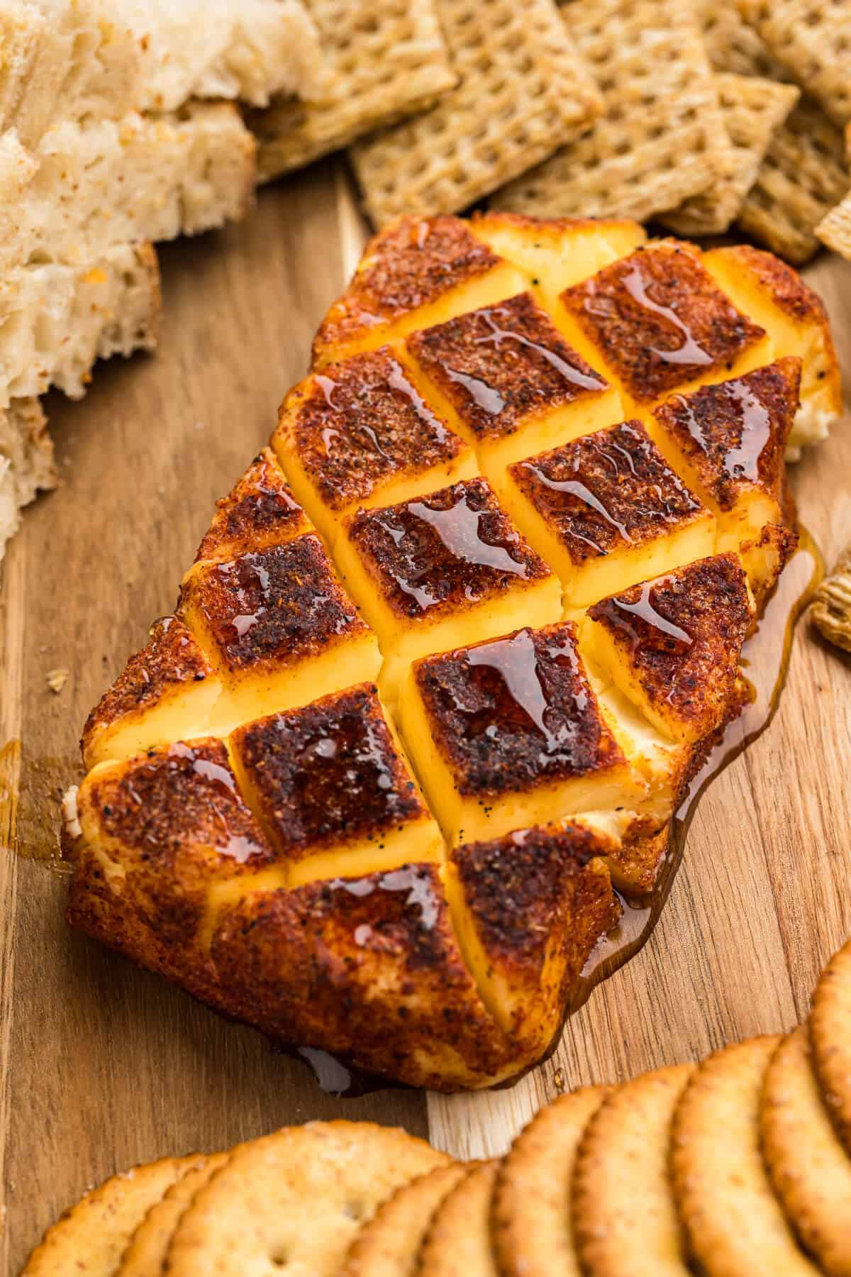 Smoked cream cheese with a cross hatch pattern and a drizzle of honey, surrounded by crackers and bread on a wooden platter.