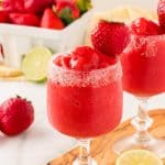Virgin strawberry daiquiris in a sugar rimmed glass, garnished with a strawberry. A quart of strawberries is in the background, and there are a few strawberries and lime wheels scattered.