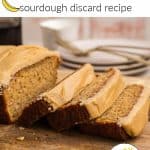A loaf of banana bread with caramel icing, with three slices laying down on a cutting board next to the loaf itself.