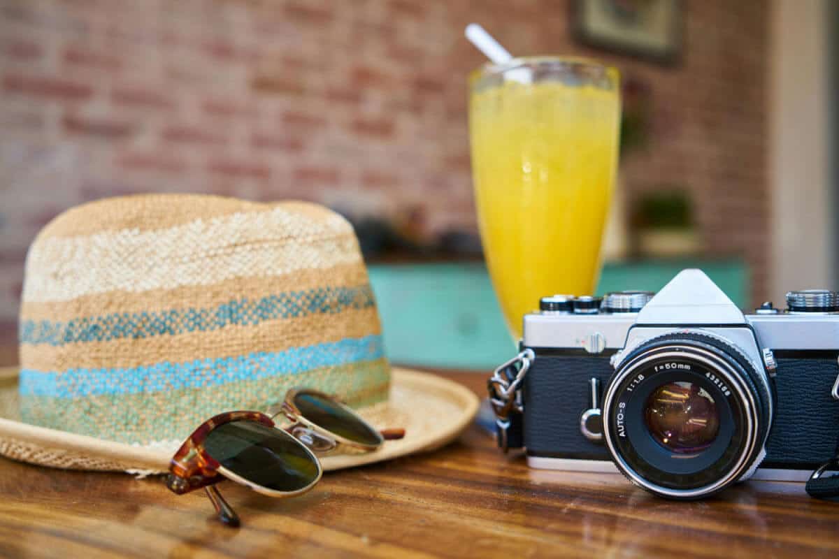 Table top with a sun hat, camera, sunglasses and a refreshing orange drink on it.