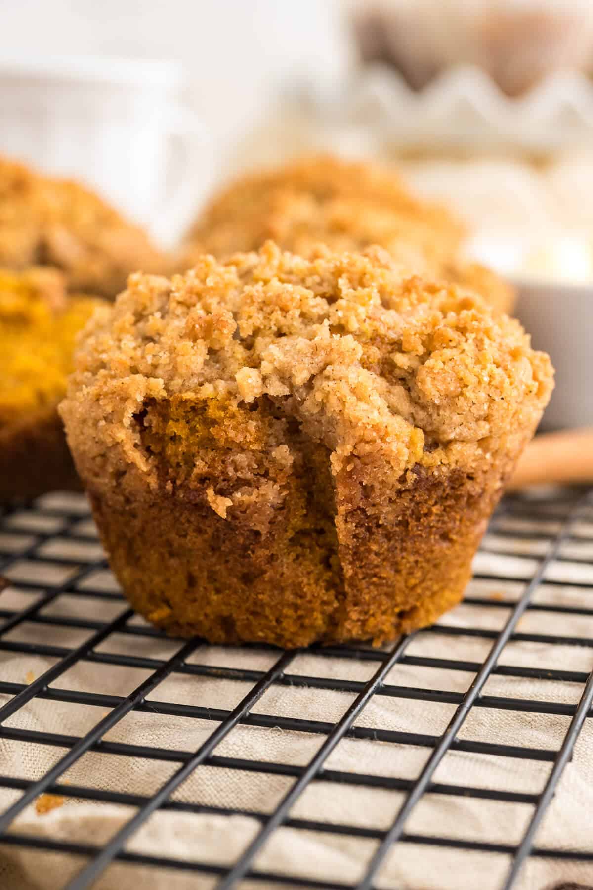 Pumpkin Muffin with Streusel topping on a. baking rack with more muffins blurred out behind it.