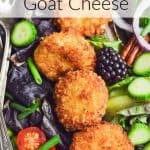 Green salad with red onion, cucumber slices, black berries, and cherry tomatoes topped with medallions of crispy fried goat cheese. Text overlay reads: Fried Goat Cheese.