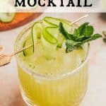 Glass of a Cucumber Lime Mocktail garnished with fresh mint and cucumber ribbons. Cucumber ribbons and fresh lime are in the background. Text overlay reads: Cucumber Mocktail