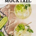 Overhead view of three cucumber mocktails. Drinks are garnished with fresh mint, and a cucumber ribbon on a gold cocktail spear. Fresh limes, mint, and cucumbers are off to the side with the edge of a striped towel with tassles. Text overlay reads: Cucumber Mocktail.