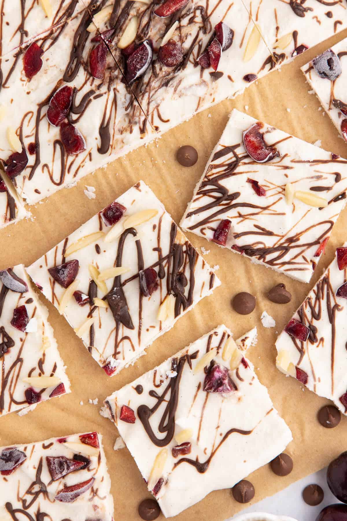 Cottage Cheese Ice Cream Bark cut into squares, a few bars pulled away from the whole piece. It is drizzled with chocolate, and topped with pieces of cherries and slivered almonds.