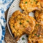 Crispy air fryer fried pork chops on a plate, garnished with fresh parsley and served on a woven placemat with a blue and white napkin.