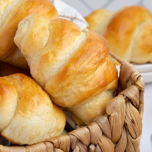 Crescent Rolls stacked in a woven basket. In the background is a plate with a roll on it.