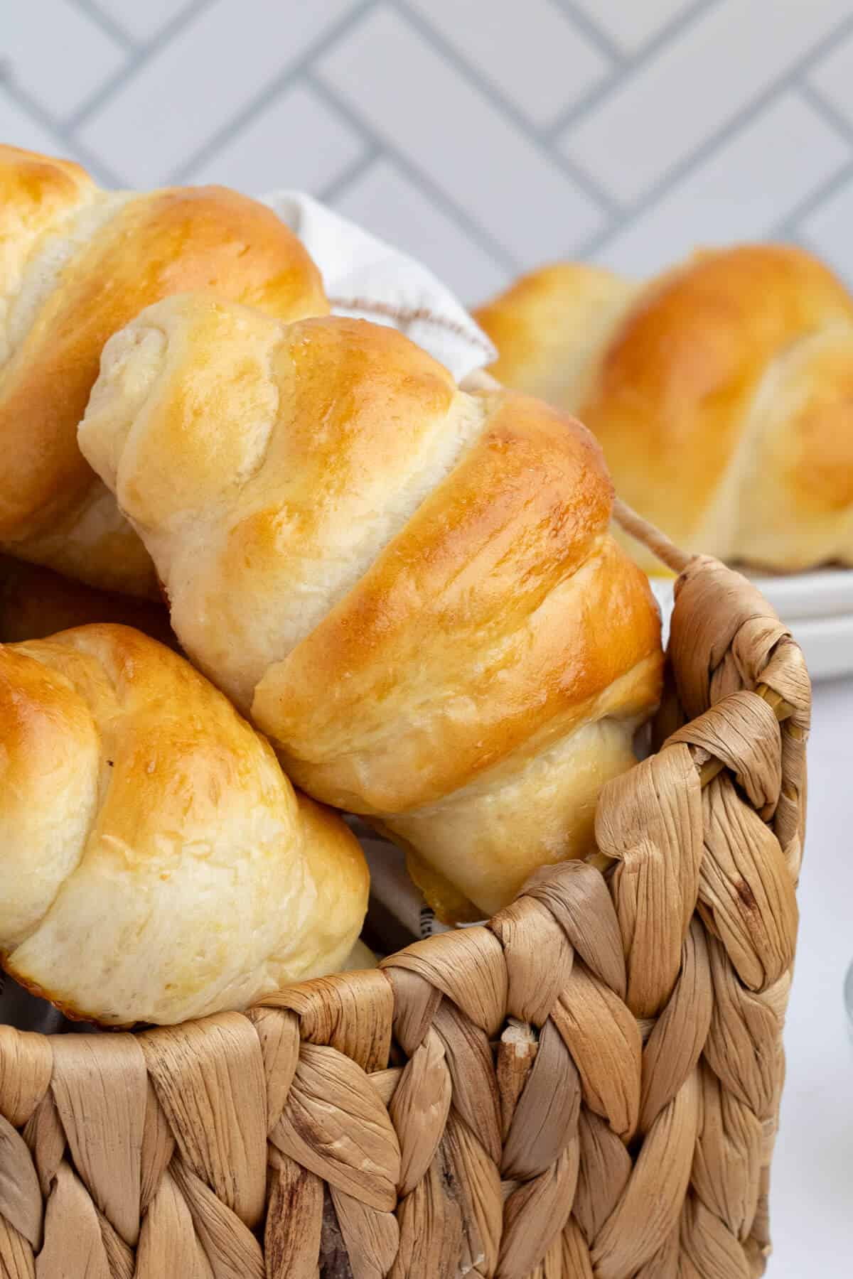 Crescent Rolls stacked in a woven basket. In the background is a plate with a roll on it.