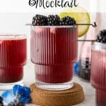 Blackberry Mocktail in a ribbed glass on a cork coaster, garnished with fresh blackberries and a lime slice, with more glasses and a carafe in the background. Text overlay reads Blackberry Mocktail.
