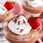 Three stemmed dessert dishes filled with Cottage Cheese Chocolate mousse, one in the front and two in the background. They are topped with whipped cream and chocolate shavings, and garnished with a sliced strawberry with the stem in tact.