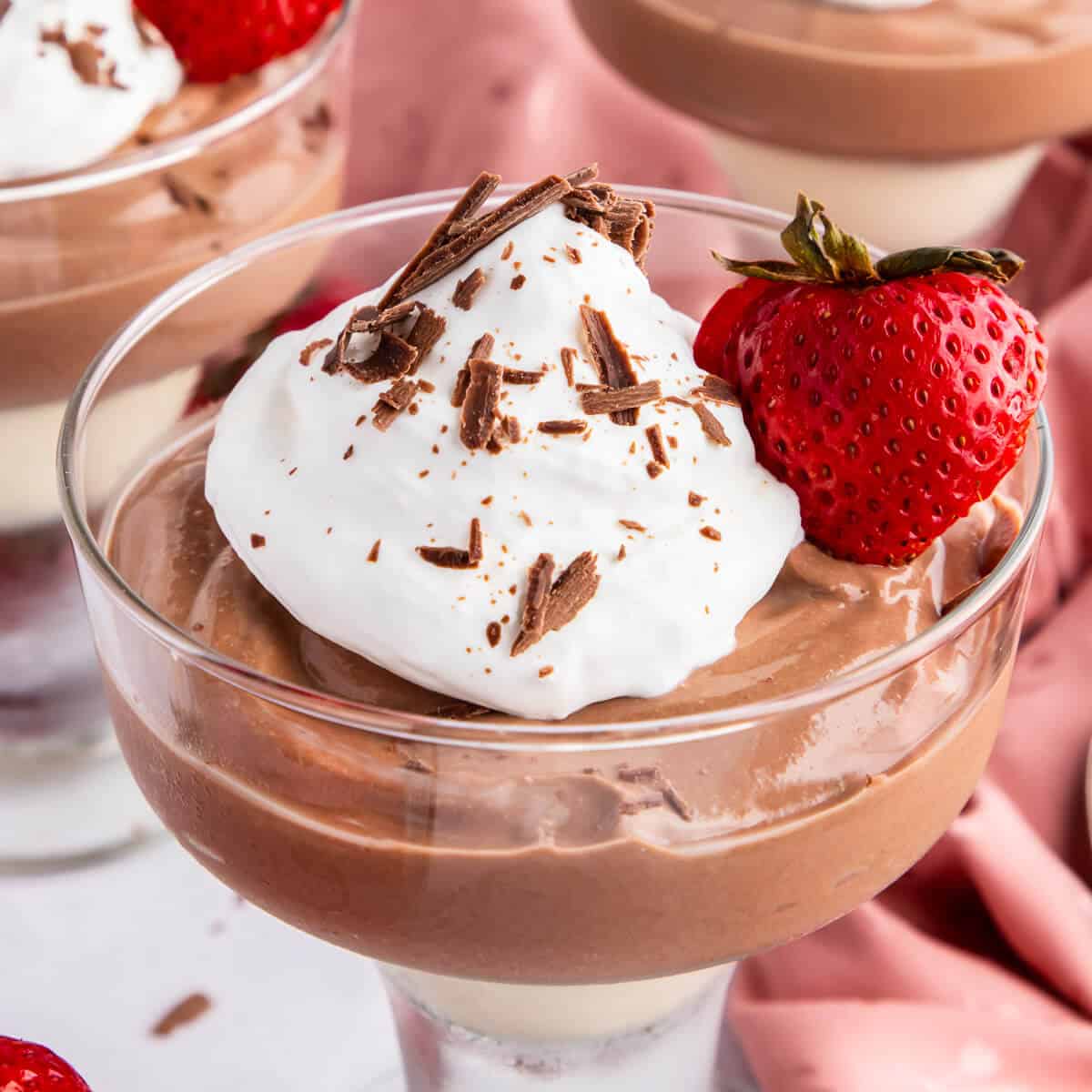 A stemmed dessert dish filled with Cottage Cheese Chocolate mousse. It's topped with whipped cream and chocolate shavings, and garnished with a sliced strawberry with the stem in tact.